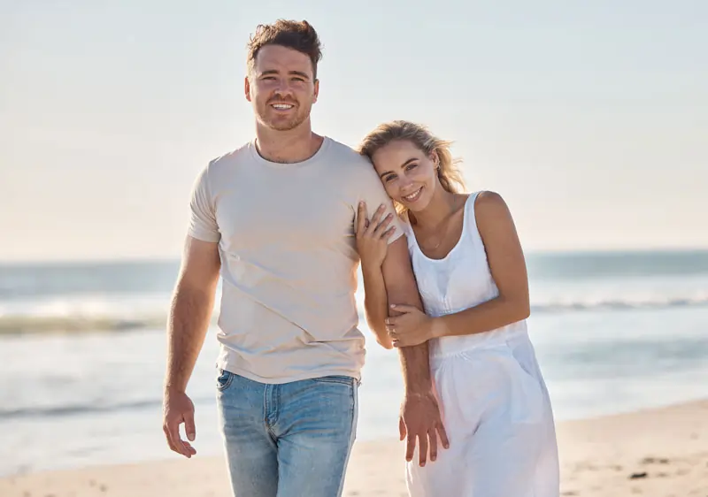 Ein Paar spaziert am Strand entlang, die Frau hält den Arm des Mannes, symbolisiert die ersten Schritte nach der Trennung und die langsame Wiederannäherung.